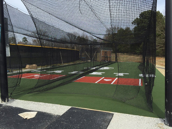 Outdoor batting cages with green synthetic turf, inlaid red batter's boxes, and black cage netting