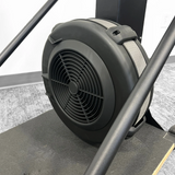 Close-up of the Echo Kodiak Echo Commercial Ski Erg 02008 flywheel with fan, gray strap, and metal frame on carpeted floor.