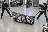 Two people lift a humanoid robot wrapped in Kodiak Sports’ Robot Capture and Containment Netting off the floor.