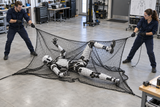Two engineers capture a humanoid robot using Kodiak Sports’ Robot Capture and Containment Netting on the workshop floor.