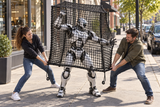 Two people use Kodiak Sports’ Robot Capture and Containment Netting Box to trap a humanoid robot on a city sidewalk.